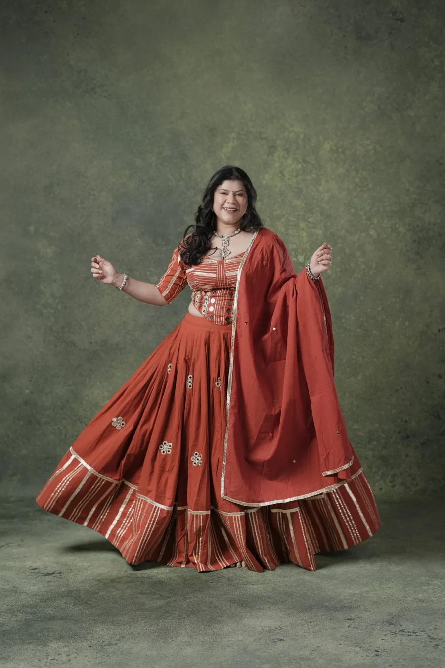 Nayana Sarma mid-performance in a red mirrorwork chaniya choli, arms raised